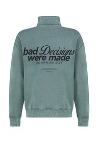 Groene fleece pullover met een hoge kraag, voorzien van gedurfde zwarte tekst op de achterkant met de tekst "slechte beslissingen zijn genomen" en extra kleinere tekst.