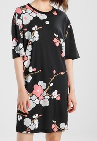 Svart blommig klänning med stora rosa och vita blommönster, korta ärmar, avslappnad passform och rund halsringning.