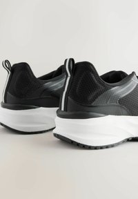 Mustad sportkingad, mis on valmistatud võrgust ja sünteetilisest materjalist, millel on paks valge tall ja hallid triibud tagaosas. Tekstuuriga must ülaosa.