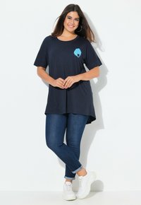 Marinblå oversized T-shirt med korta ärmar, med en blå grafisk hjärt-design på bröstet; matchad med mörka jeans och vita sneakers.