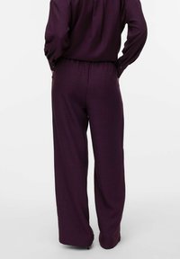 Loose-fitting, wide-leg pants in deep purple textured fabric, featuring an elastic waistband and button detail on the back.
