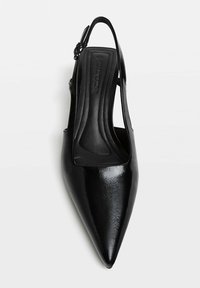 Svart lackläder slingback-sko med spetsig tå, justerbar spänne och vadderad innersula, sedd ovanifrån.