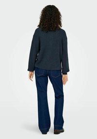 Pull gris foncé texturé avec des manches larges associé à un jean bleu évasé. L'ensemble présente une coupe décontractée et un minimum de détails.