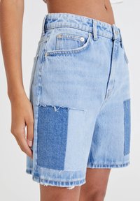 Shorts en denim bleu clair avec un design patchwork dans différentes nuances de bleu. Présente un ourlet effiloché et une coupe classique à cinq poches.