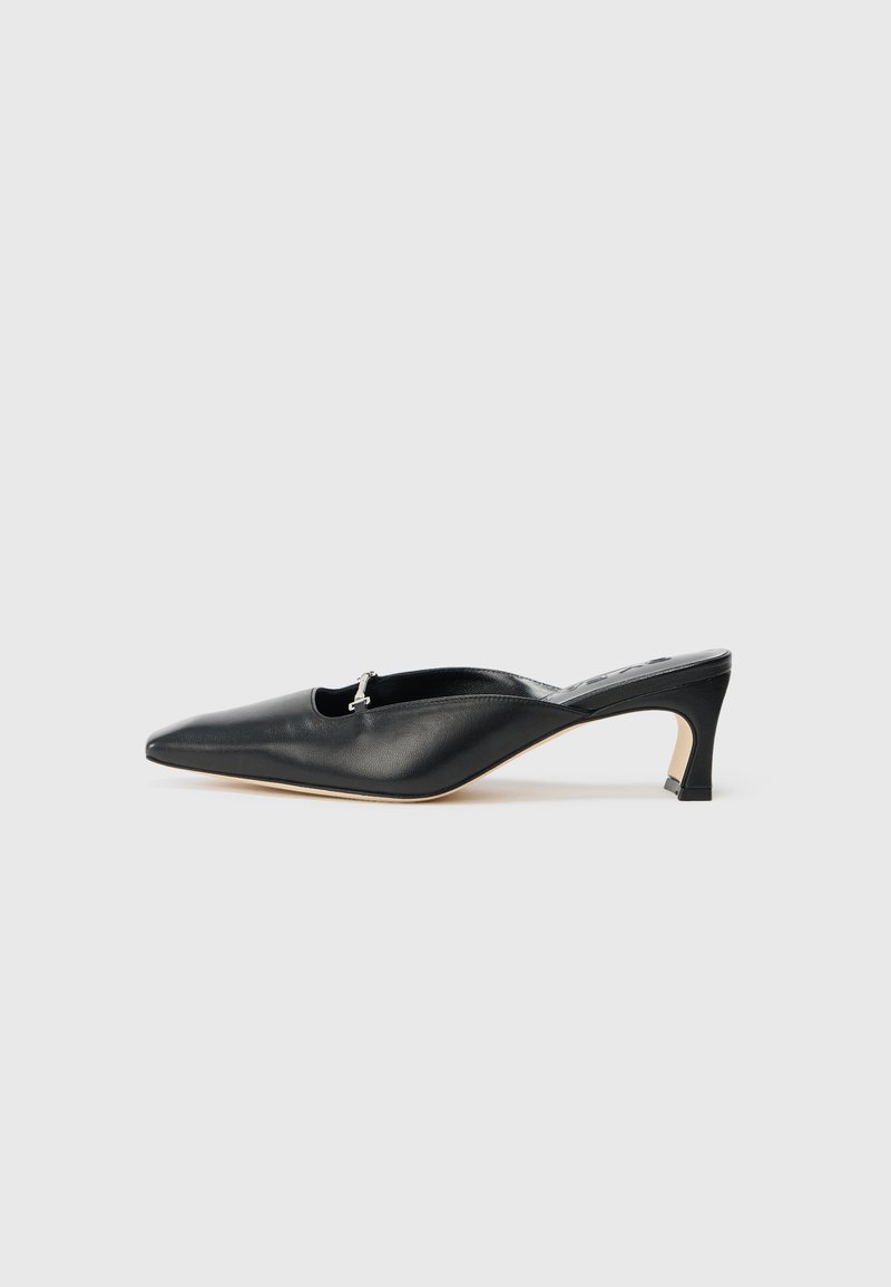 Scarpa slingback in pelle nera con punta affusolata, tacco basso e un dettaglio in acciaio inox all'apertura. Texture liscia, design minimalista.