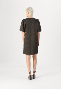 Vestido de manga curta em tecido castanho texturizado, com corte reto e uma costura nas costas. Usado com sandálias de salto preto.