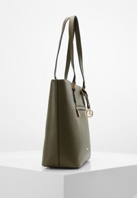 Sac fourre-tout en similicuir vert olive avec une finition texturée, deux longues poignées et des accents en métal doré, doté d'une poche zippée à l'avant.