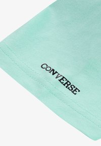 Mintgrønn bomulls T-skjorte med sømt kant og svart "CONVERSE" logo nederst til venstre. Glatt tekstur.