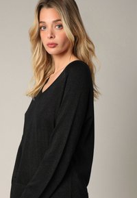 Zwarte, ruime trui met een V-hals en lange mouwen, met een subtiele glansstructuur. Rechte snit en zacht materiaal.