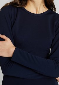 Laivastonsininen pitkähihainen paita, jossa on pyöreä pääntie ja sileä pinta. Tiukasti istuvat hihat ja vartalo ilman näkyviä kuvioita tai korostuksia.