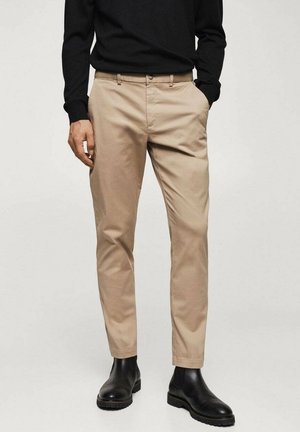 Chinos beige con una vestibilità slim, realizzati in morbido cotone, dotati di passanti per la cintura e tasche anteriori, abbinati a stivaletti neri.