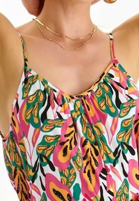 Tuote: Hihaton paita, jossa on eläväinen kukkakuosi vaaleanpunaisena, vihreänä, oranssina ja mustana valkoisella taustalla. Kevyt kangas ja kootut yksityiskohdat kauluksessa.