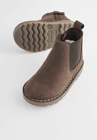 Stivali alla caviglia in suede marrone con pannelli elastici laterali, dettagli cuciti e suole in gomma texture. Due stivali mostrati da più angolazioni.