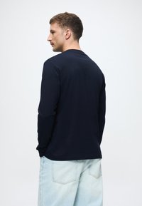 Granatowa koszula z długim rękawem, wykonana z bawełny, z okrągłym dekoltem i luźnym krojem. W połączeniu z jasnoniebieskimi dżinsami.