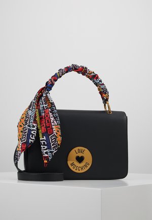 Sac bandoulière noir Love Moschino avec un emblème doré en forme de cœur et un foulard à imprimé texte multicolore noué autour de l’anse, présenté sur un socle blanc.