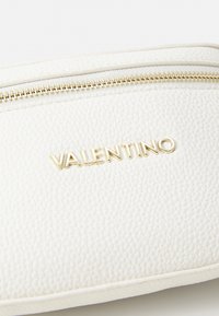 Balta odinė zip piniginė su tekstūruotu paviršiumi ir auksiniu "Valentino" logotipu. Auksinės zip užtrauktuko detalės papuošia dizainą.
