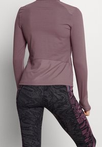 Long-sleeve top in mauve fabric with textured shoulder detail, paired with fitted black leggings featuring dark floral patterns and pink accents.