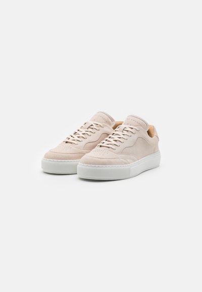 Zapatillas de ante beige con puntera redonda, diseño con cordones y suela de goma blanca. Presenta perforaciones en la caja de los dedos y una estética minimalista.