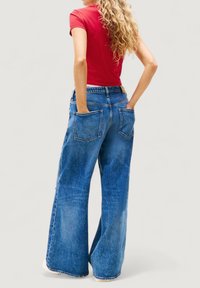 Jeans in denim blu a gamba larga con una leggera scoloritura, due tasche posteriori e orlo grezzo. Abbinati a una maglietta rossa aderente a maniche corte.