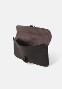 Svart läderväska med en rundad form, mjukt grått inre och framknäppning. Slät ytstruktur med minimal hårdvara.