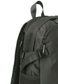 Sac à dos gris foncé en tissu texturé. Il dispose de deux zips, de bretelles réglables, d'une poche latérale en filet et d'une poignée de transport sur le dessus.