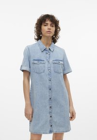 Robe chemise en denim bleu clair avec des manches courtes, devant à boutons et deux poches poitrine. Texture douce avec une coupe décontractée et des manches roulables.