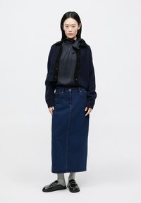 Ναυτικό κοντό ζακέτα πάνω από γκρι μπλούζα, συνδυασμένο με μακριά τζιν φούστα. Μαύρα μοκασίνια και γκρι κάλτσες ολοκληρώνουν την εμφάνιση. Λεία υφάσματα και σκούρα χρώματα.