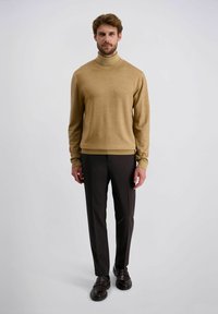 Beige coltrui van een zachte stof, gecombineerd met donkere, op maat gemaakte broeken en bruine schoenen. Eenvoudig ontwerp, aansluitende silhouet.