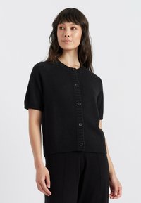 Schwarze Kurzarm-Cardigan aus weichem Stoff, mit Rundhalsausschnitt und Knopfleiste, die am Rand mit strukturiertem Rippenmuster versehen ist.