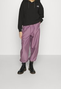 Svart texturerad hoodie, löst sittande lila byxor med elastisk midja och svarta snörkängor med tjock sula.