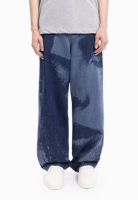 Szerokie spodnie dżinsowe o gradacyjnym niebieskim wzorze z teksturowanym motywem, wykonane z denimu, o luźnym kroju i widocznych przeszyciach.