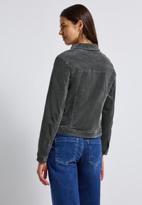 Šedá kordová bunda se strukturovaným designem, dlouhými rukávy, límcem a zapínáním na knoflíky, v kombinaci s modrými džínami.