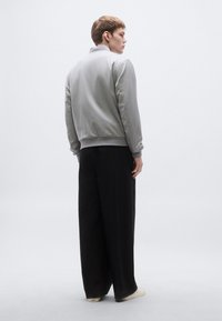 Szürke bomber dzseki gallérral és bordázott mandzsettákkal, széles fekete nadrággal és világos színű lábbelivel párosítva. Minimalista dizájn, sima textúra.