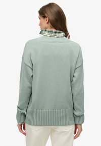Lichtgroene gebreide trui met geribbelde zoom en manchetten, met een geruite kraag die eronderuit piept, met een gestructureerde stof.