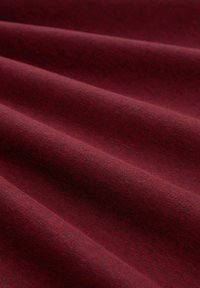 Bordeaux stof met een zachte, textuurachtige oppervlakte, die subtiele variaties in tint en zachte vouwen vertoont die diepte en beweging creëren.