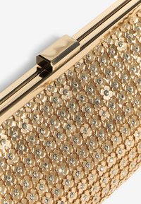 Clutch dorado con una superficie texturizada adornada con pequeños patrones de círculos metálicos y piedras de strass incrustadas, con cierre de pestillo.