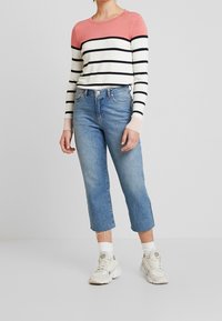 Randig tröja med rosa axlar, blå avkortade jeans och vita sneakers. Slät tyg, klassisk passform och slitna detaljer på jeansen.