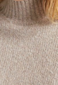 Beige geribbelde gebreide coltrui met een zachte textuur en een strakke pasvorm, die een subtiele, neutrale kleurtoon laat zien.