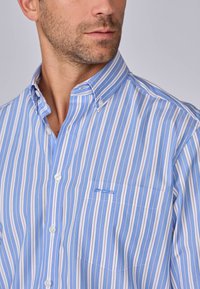 Chemise à manches longues à rayures bleues et blanches avec un col, dotée d'une poche poitrine et d'un subtil détail de broderie. Tissu en coton doux.