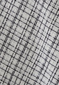 Tessuto tessile con un motivo a griglia intrecciato in nero su uno sfondo bianco, con texture varie e bordi sfilacciati.