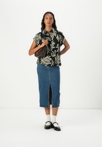 Zwart shirt met korte mouwen met een crèmekleurig bladcircus, gecombineerd met een jeansrok tot de knie met een voorkap. Zwarte handtas en schoenen.