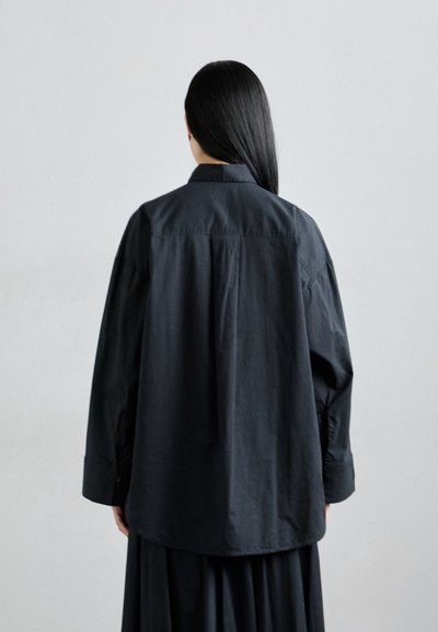 Black oversized shirt made of cotton, featuring a back yoke, long sleeves, and button cuffs. Smooth texture with a relaxed fit.