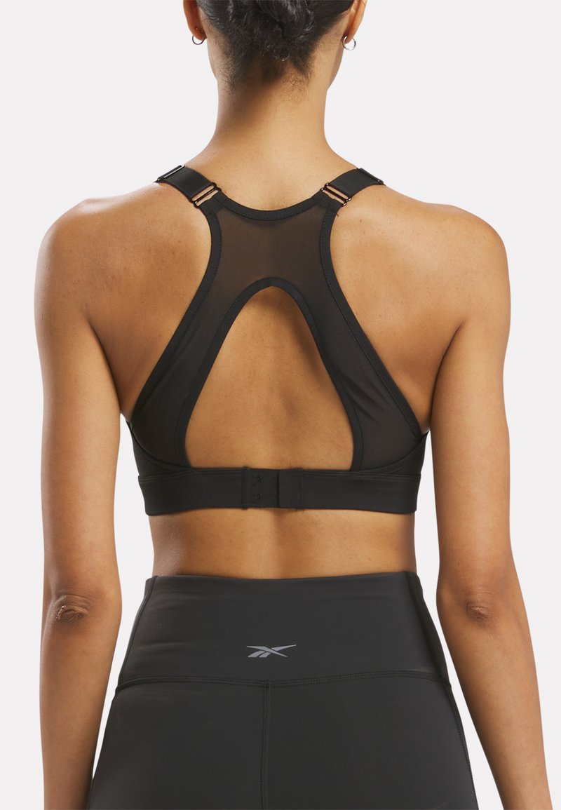 Sostén deportivo negro con paneles de malla, espalda en forma de U y tirantes ajustables. Presenta cierres con broches en la parte posterior. Textura de tela suave.