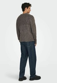 Pull en laine marron avec un col rond et des poignets côtelés, associé à un jean bleu foncé ample et des chaussures noires à semelle épaisse.