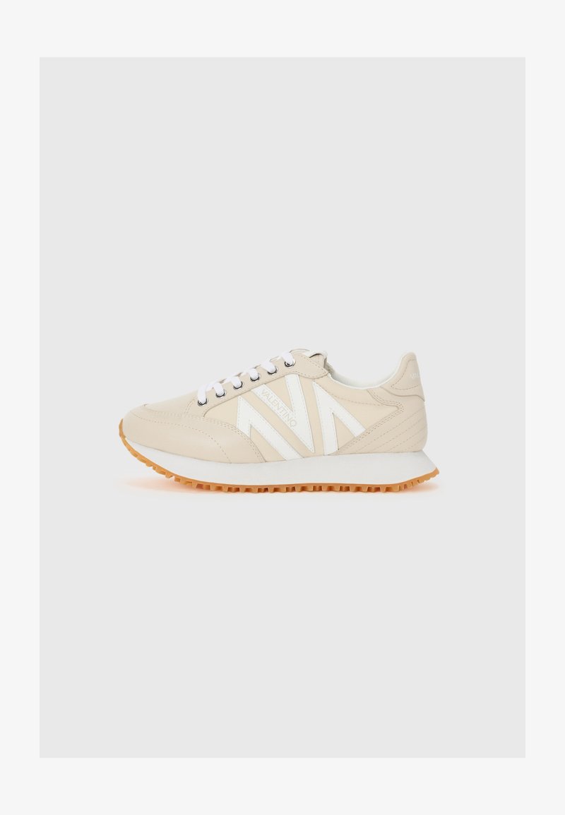 Baskets de sport beige avec accents blancs, tige en cuir texturé, devant à lacets et semelle en caoutchouc avec un motif de semelle. Design minimaliste.