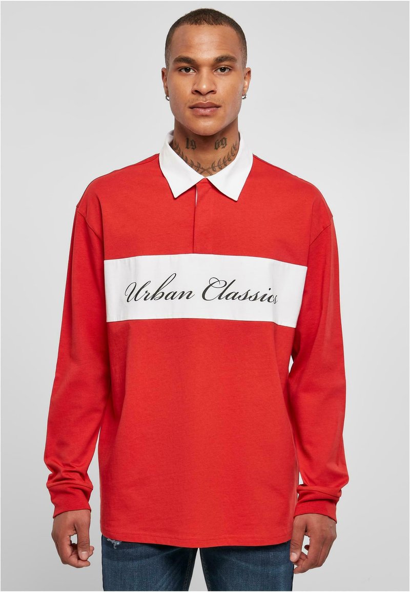 Polo roșu cu mânecă lungă, decorat cu o bandă orizontală albă pe care este inscripționat textul "Urban Classics", guler clasic și țesătură moale din bumbac.