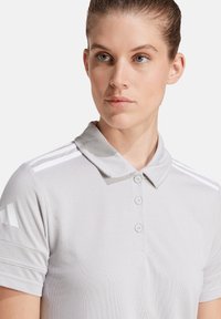 Grijze poloshirt gemaakt van ademend materiaal, met een klassieke kraag, drie knopen en witte strepen op de schouders.