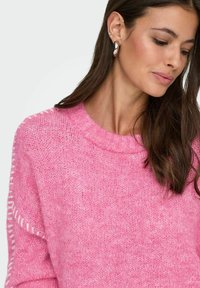 Roze gebreide trui met een ronde hals, zichtbare stiksels op de mouwen en een zachte, gestructureerde stof.