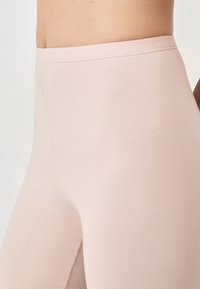 Leggings rosa chiaro con una texture liscia, dotati di un alto punto vita e design aderente, adatti per abbigliamento sportivo o outfit casual.