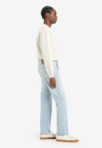 Light beige sweatshirt, light blue straight-leg jeans, and cream sneakers with white accents. Smooth texture, casual fit, and minimalist design.